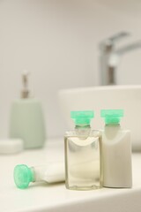 Mini bottles of cosmetic products on white countertop in bathroom