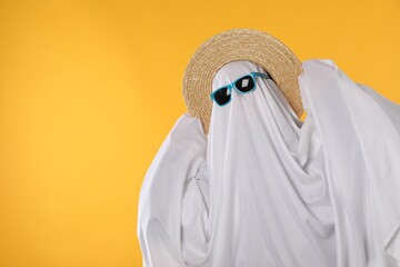 Person in ghost costume, sunglasses and straw hat on yellow background, space for text