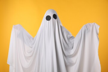 Creepy ghost. Person covered with white sheet on yellow background