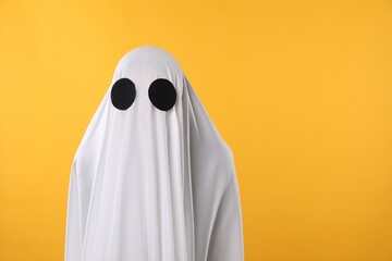 Creepy ghost. Person covered with white sheet on yellow background, space for text