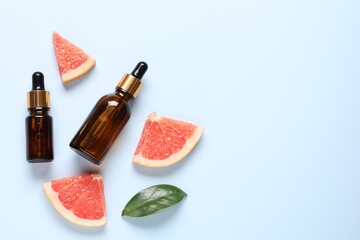 Grapefruit essential oil in bottles, leaf and cut fruit on light blue table, flat lay. Space for...