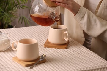 Woman pouring aromatic tea into cup at table, closeup