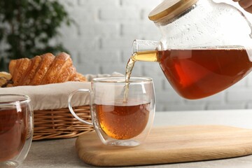 Pouring aromatic tea into glass cup at light grey table, closeup