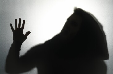 Silhouette of ghost behind glass against light grey background