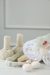 Beautiful spa composition. Towels, herbal bags, soap bars and burning candles on white wooden table
