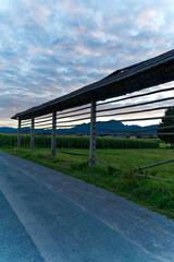 Hayrack at farmland between villages of Zabnica and Sutna with corn field and houses in the background on a blue cloudy summer evening. Photo taken August 10th, 2023, Zabnica, Kranj, Slovenia.