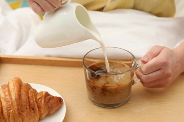 Woman pouring milk into cup with hot drink in bed, closeup