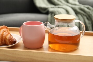 Aromatic tea in teapot, cup and tasty croissant on table indoors