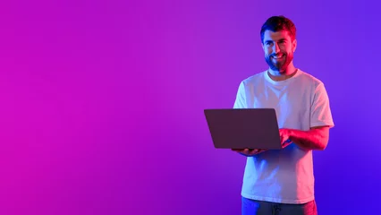  Young caucasian guy using laptop in studio with neon light © Prostock-studio