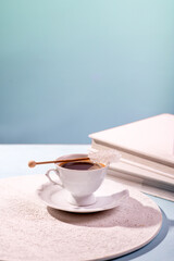 White cup and saucer with black coffee on a light table. Place for text. Coffee with sugar crystal on a stick.