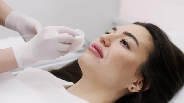A female cosmetologist in white gloves prepares a syringe and lips of a young patient for cosmetic injections. Cosmetic injections, rejuvenation, cosmetologist services.