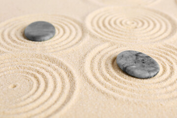 Fototapeta na wymiar Zen garden stones on beige sand with pattern, closeup
