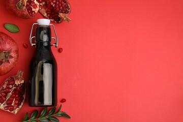 Tasty pomegranate sauce in bottle, leaves and fruits on red background, flat lay. Space for text