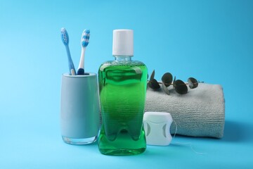 Fresh mouthwash in bottle, dental floss and toothbrushes on light blue background
