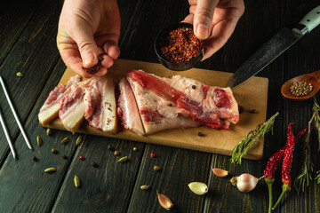 The chef seasones lard with spices on a wooden cutting board. Concept of preparing delicious pork...