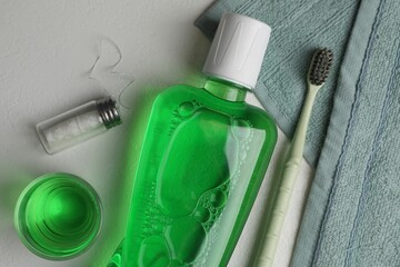 Fresh mouthwash in bottle, glass, toothbrush and dental floss on light background, flat lay