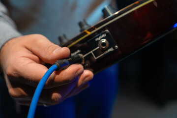 Close up man hand sticking plug to guitar in concert hall. Unrecognizable person connecting instrument in recording studio. Unknown sound engineer preparing electric guitar for playing.