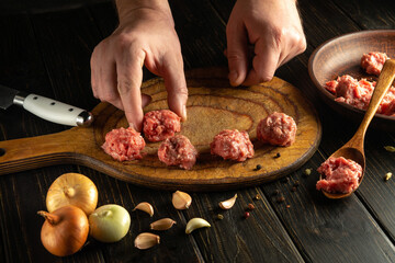 The cook hand places a raw meatball on the kitchen board. Cooking meat on the kitchen table with spices. Cooking, recipes and low key food concept.