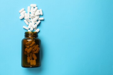 Bottle and vitamin capsules on light blue background, top view. Space for text