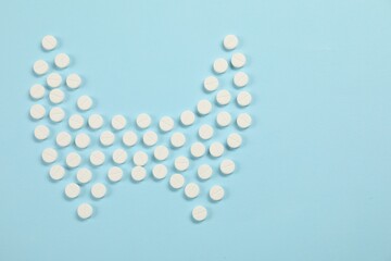 Endocrinology, Shape of thyroid gland made of pills on light blue background, flat lay. Space for text