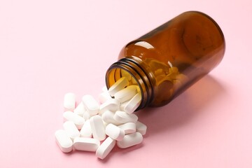 Bottle and vitamin capsules on pink background