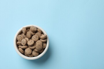 Vitamin pills in bowl on light blue background, top view. Space for text
