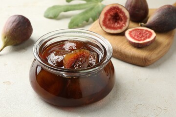 Jar of tasty sweet jam and fresh figs on white table