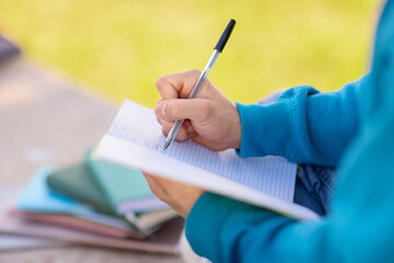 Closeup of notebook in student guy's hands taking notes outdoors - obrazy, fototapety, plakaty