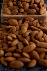 Perfect almonds in close-up on a gray textured background are scattered on a square-shaped wooden plate. Raw peeled almonds piled on the table, top view