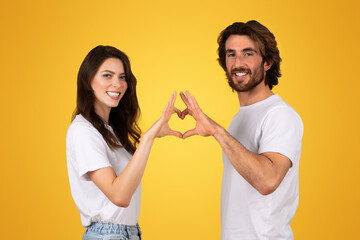 Radiant young couple creating a heart shape with their hands, smiling broadly in white t-shirts