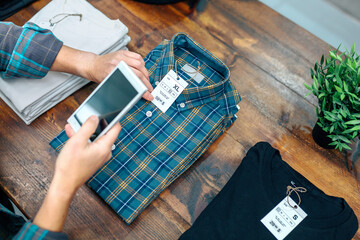 Unrecognizable woman customer holding cellphone while scan label with price and size of plaid shirt...