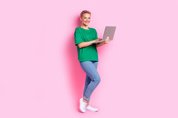 Full size photo of intelligent pretty cute girl dressed green t-shirt jeans typing email on laptop isolated on pink color background