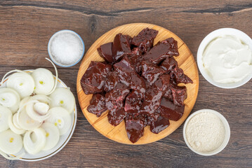Top view of raw beef liver pieces, onion rings, salt and sour cream.