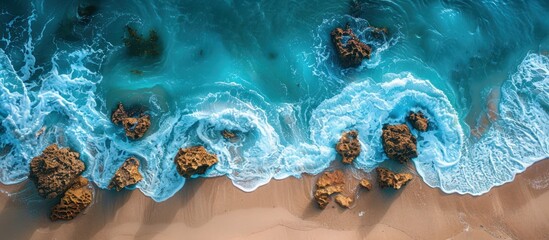This aerial view showcases a beach with waves crashing against rocks, creating a dynamic scene of natural beauty.