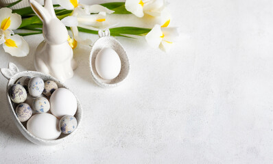 Fototapeta premium Easter white holiday card. Natural colors eggs in figured bowls, ceramic bunny, flowers. Copy space.