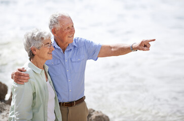 Senior, couple and point at beach with smile for retirement vacation or anniversary to relax with love, view and commitment with support. Elderly man, woman and together by ocean for peace on holiday