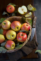 Apples in a basket on a wooden table. Fresh red apples with green leaves on a black background. Fruits. View from above.