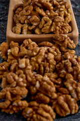 Top view of the halves of walnut kernels in a wooden plate on a gray background. Large walnuts in a wooden cup on a textured background