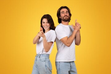 Confident young couple in white t-shirts standing back to back, giving thumbs up