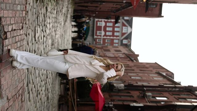 Vertical - Blonde Woman In Formal Coat And White Pants Posing On Cobbled Street In Portland, Maine. slow motion