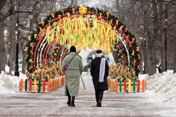 Russian Maslenitsa, two women walking on background of shrovetide decorations in spring city
