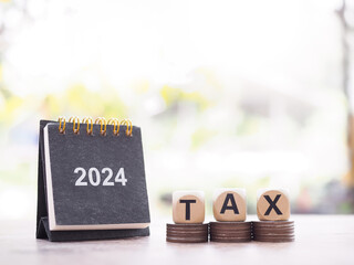 2024 desk calendar, Wooden block with word TAX on stack of coins. The concept of saving money for...