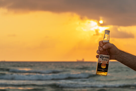 Ashdod, Israel, July 2023: A bottle of cold beer Corona Extra in male hand on the beach golden hour