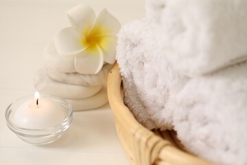 Fototapeta na wymiar Spa composition. Rolled towels, massage stones, burning candle and plumeria flower on table, closeup