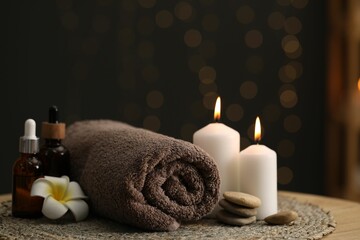Spa composition. Rolled towel, cosmetic products, stones, burning candles and plumeria flower on table indoors, closeup. Space for text