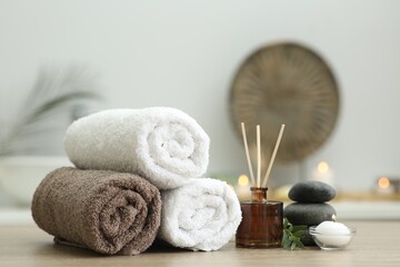 Spa composition. Rolled towels, aroma diffuser, massage stones and burning candle on wooden table...