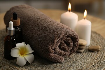 Fototapeta na wymiar Spa composition. Rolled towel, cosmetic products, stones, burning candles and plumeria flower on table, closeup