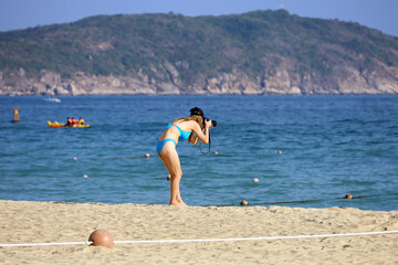 Girl in blue bikini taking photos on camera standing on sea beach