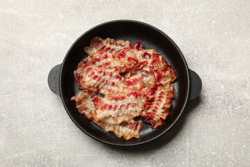 Delicious bacon slices in frying pan on grey table, top view