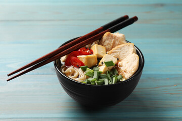 Delicious ramen and chopsticks on light blue wooden table. Noodle soup